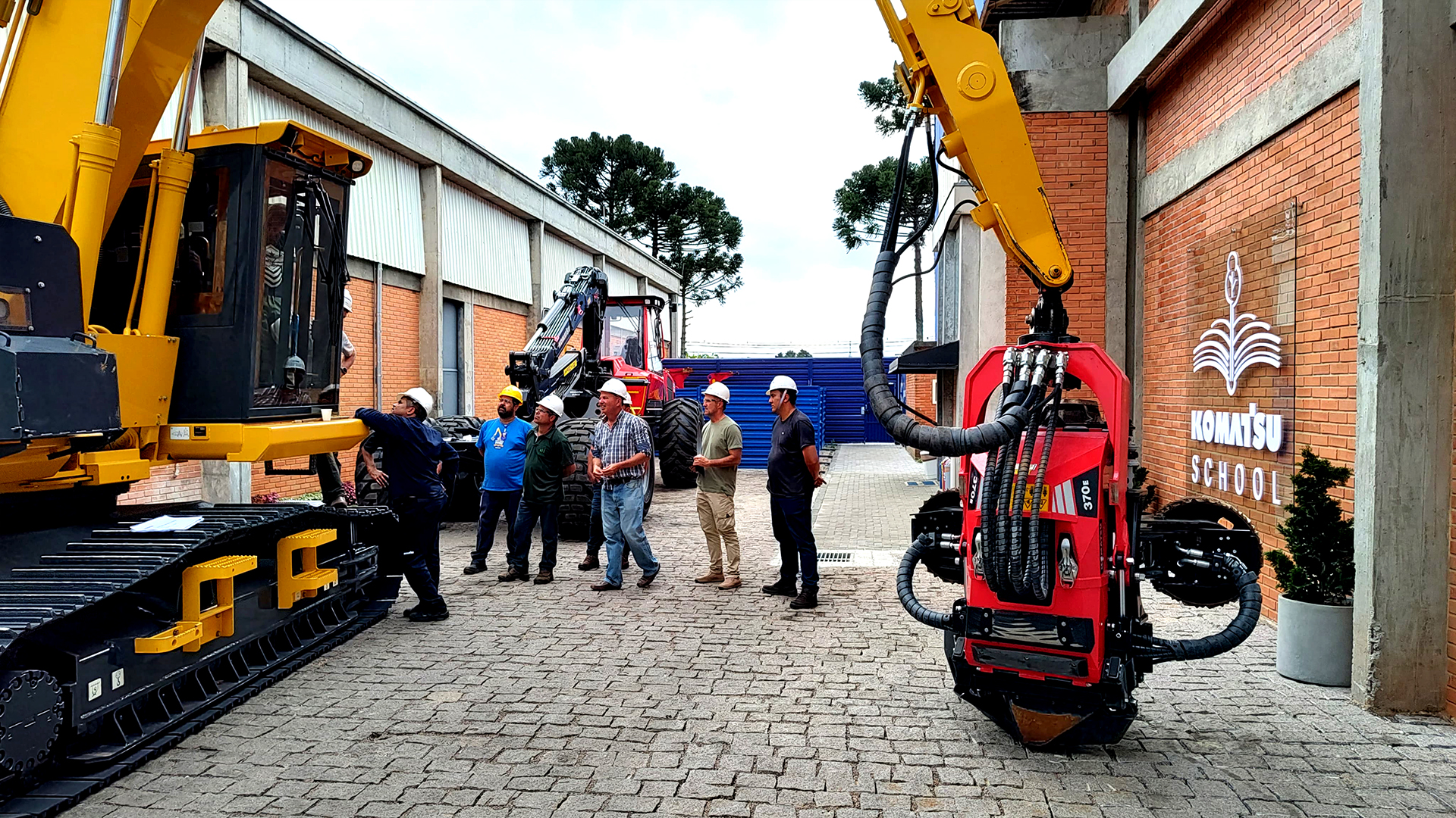 Turma da Komatsu School no pátio de máquinas, diante da fachada com a marca da escola
